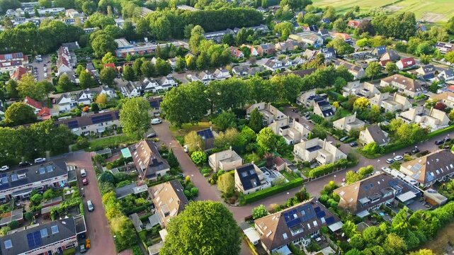 Beautiful aerial of a peaceful suburban neighborhood with solar panels on the rooftops of houses. Lush and green trees grow around the neighborhood while the sun shines brightly on this summer day