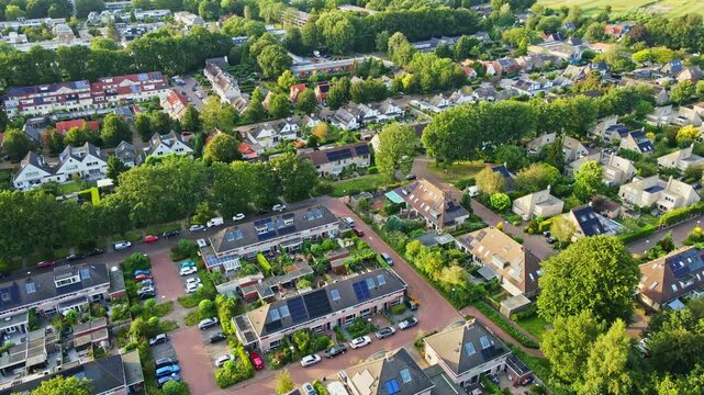 Aerial dolly of a beautiful suburban neighborhood with photovoltaic solar panes on the roofs of homes. The suburbs are filled with lush and green trees and it's a sunny summer day