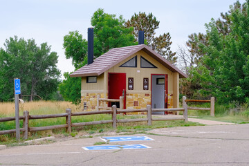Outdoor restroom facility with handicapped parking spaces surrounded by trees and greenery along a...