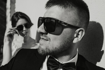 A man wearing sunglasses and a bow tie stands next to a woman. Scene is formal and elegant, as the man