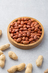 Whole and raw peanuts in a wooden bowl on a gray background.