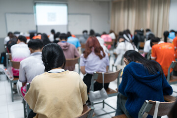 Selective focused high school or university students are intently writing on their answer sheets during a final exam in the classroom.