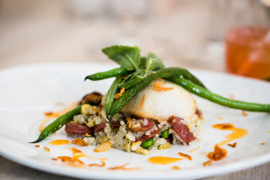 Close-up of black cod fish filet with a Chinese sausage and rice side dish and green beans on a dinner plate, at an event, Canada