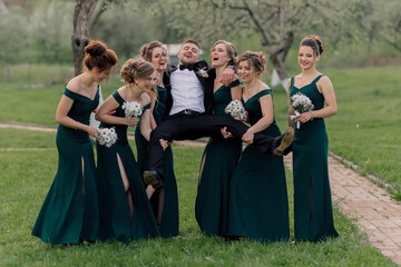 A group of women are posing for a picture with a man in a suit. The man is lifting one of the women, and the other women are standing around him. Scene is lighthearted and fun