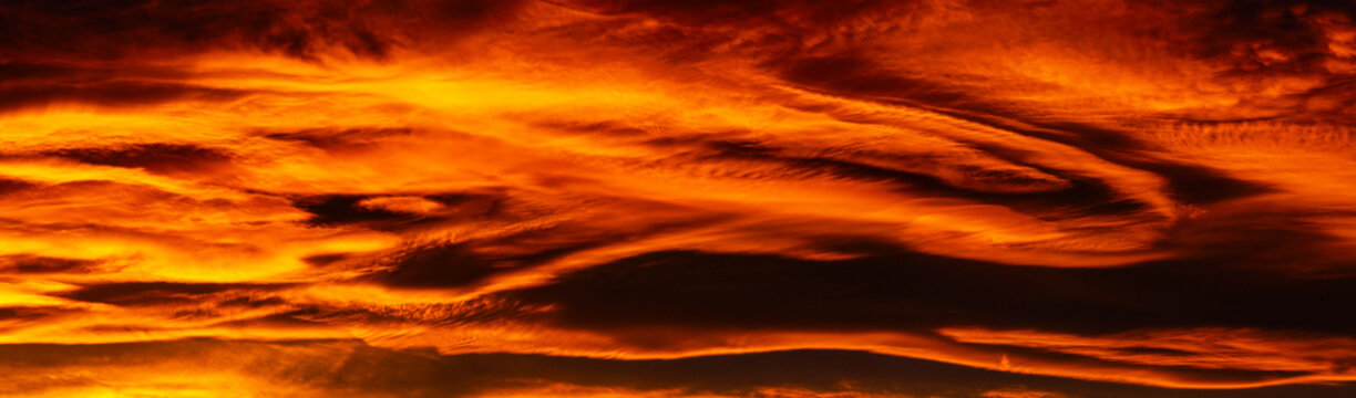 Panoramic of colorful red and gold cloud formations in a dramatic sky at twilight; Calgary, Alberta, Canada