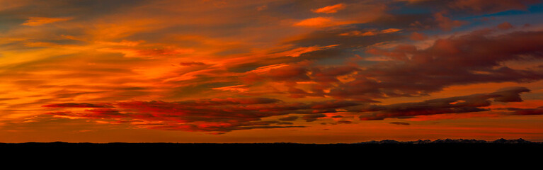 Panoramic of colorful red and orange cloud formations creating a dramatic sky at twilight with a silhouetted horizon; Calgary, Alberta, Canada