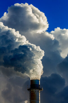 Close-up of an electrical plant's stack with large clouds of exhausts and blue sky; East of Calgary, Alberta, Canada