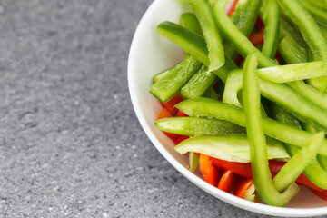 Chopped red and green bell peppers in white ceramic bowl.Vibrant colors dinner salad textures. Empty copy space kitchen counter background.