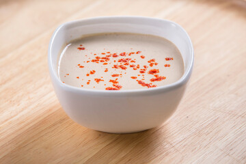 tahini sauce in a small bowl served on a wooden table spiced with paprika powder on it