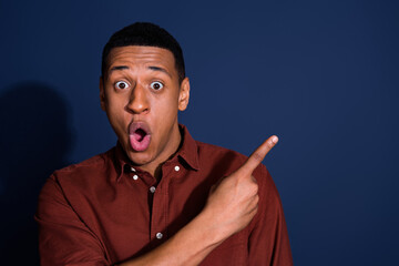 Photo portrait of nice young man point shock empty space wear trendy brown outfit isolated on dark blue color background