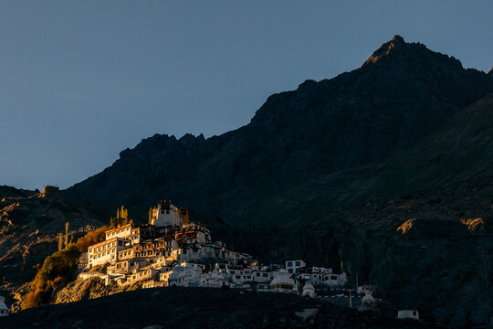 Diskit Gompa (Monastery) illuminated by warm sunlight with the mountains dark in shadows in the Nubra Valley; Leh, Ladakh, India