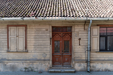 A weathered wooden house with ornate doors and a tiled roof in a quiet neighborhood during daytime hours