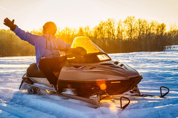 Man enjoys an outing riding his snowmobile at sunset and waving hello on a beautiful winter day; Bon Accord, Alberta, Canada