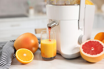 Modern juicer, oranges, grapefruits and glass on white marble table in kitchen