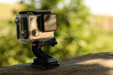 Modern action camera with mount on wooden surface outdoors, closeup. Space for text