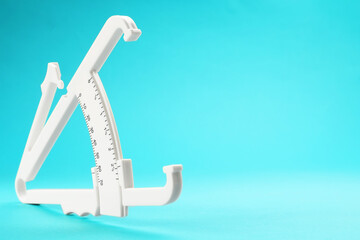 Plastic body fat caliper on light blue background, closeup. Space for text
