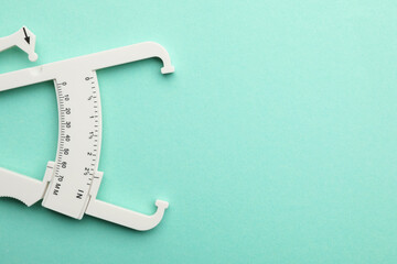 Plastic body fat caliper on turquoise background, top view. Space for text