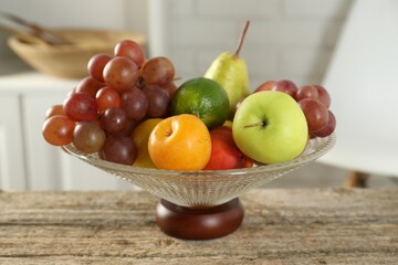 Glass vase with different fresh fruits on wooden table