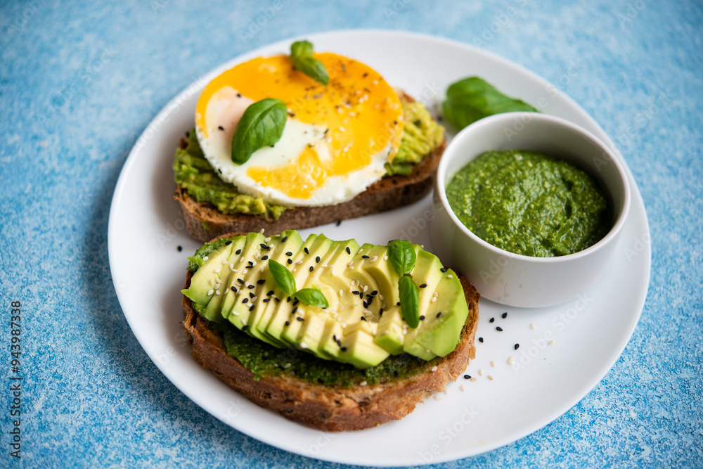 Wall mural two toasts with avocado, egg and pesto sauce. a balanced breakfast for a healthy and keto diet.