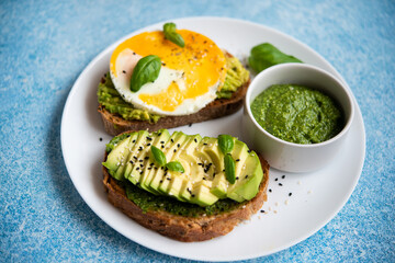 Two toasts with avocado, egg and pesto sauce. A balanced breakfast for a healthy and keto diet.