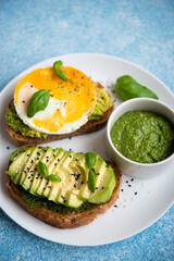 Two toasts with avocado, egg and pesto sauce. A balanced breakfast for a healthy and keto diet.