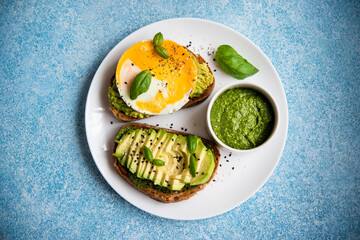 Two toasts with avocado, egg and pesto sauce. A balanced breakfast for a healthy and keto diet.