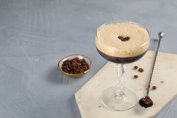 Fresh coffee cocktail in glass, beans and mixing spoon on grey table, space for text