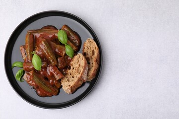 Tasty stew with okra, tomato sauce, bread and basil on white table, top view. Space for text