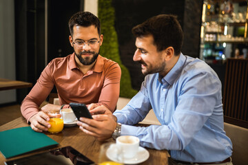 Two colleagues met at the coffee shop to discuss about work. Working on tablet and phone.