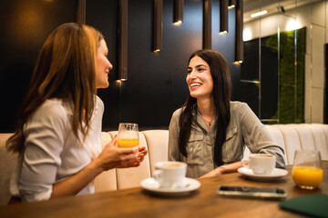 Two girl friends met at the cafe. Drinking coffee and orange juice. They are talking, gossiping and having fun time.
