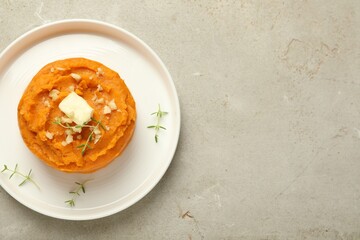 Plate with tasty mashed sweet potato, butter, thyme and walnuts on grey textured table, top view. Space for text