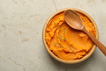 Tasty mashed sweet potato and thyme in bowl on grey textured table, top view. Space for text