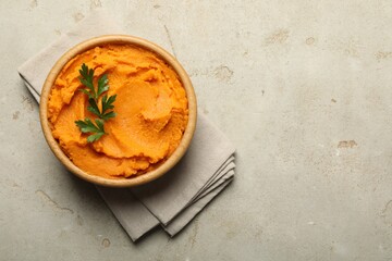 Tasty mashed sweet potato and parsley in bowl on grey textured table, top view. Space for text