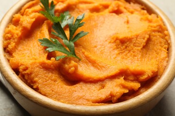 Tasty mashed sweet potato and parsley in bowl on table, closeup