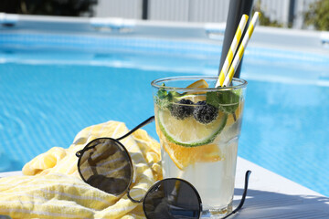 Tasty cocktail in glass and sunglasses near swimming pool outdoors