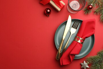 Beautiful Christmas setting with plate, elegant cutlery and festive decor on red table, flat lay....