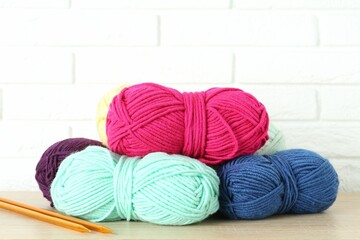 Skeins of yarn and knitting needles on wooden shelf near white brick wall