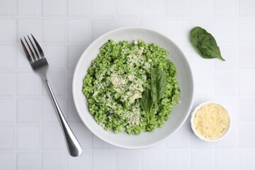 Delicious spinach risotto with parmesan cheese served on white tiled table, flat lay