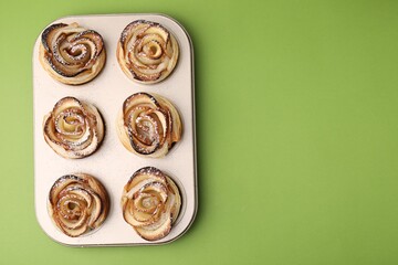 Freshly baked apple roses on green background, top view with space for text. Puff pastry