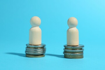 Financial equality. Wooden figures on similar stacks of coins on light blue background