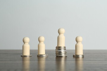 Financial inequality. One wooden figure with bigger stack of coins than others on table