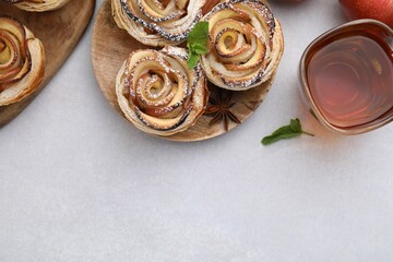 Freshly baked apple roses, ingredients and tea on light table, flat lay. Space for text