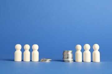 Financial inequality. Wooden figures and stacked coins of different height against blue background