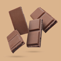 Pieces of sweet chocolate falling on dark beige background