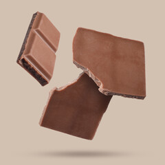 Pieces of sweet chocolate falling on beige background