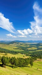 Naklejka premium Majestic mountains rise in the background while the vibrant valley unfolds below, filled with green trees and a clear blue sky scattered with white clouds