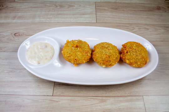 A crisp fried India snack called Sabudana Vada made from tapioca seeds, roasted peanuts, boiled potato and herbs served in a terracotta bowl placed on a white background