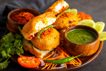 selective focus of Mumbai's famous street food delicious Vada Pav, With coriander leave chutney, tomato sauce, dry garlic chutney and fried chilli. 
