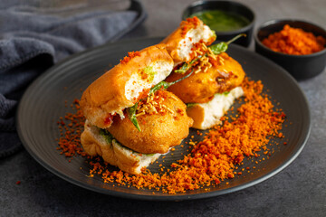 selective focus of Mumbai's famous street food delicious Vada Pav, With coriander leave chutney, tomato sauce, dry garlic chutney and fried chilli. 