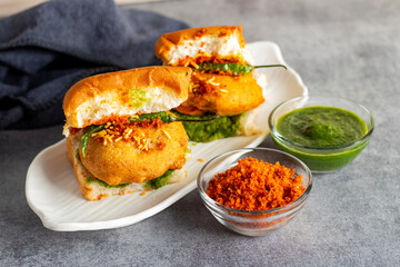 selective focus of Mumbai's famous street food delicious Vada Pav, With coriander leave chutney, tomato sauce, dry garlic chutney and fried chilli. 